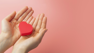 Mani tengono oggetto a forma di cuore rosso