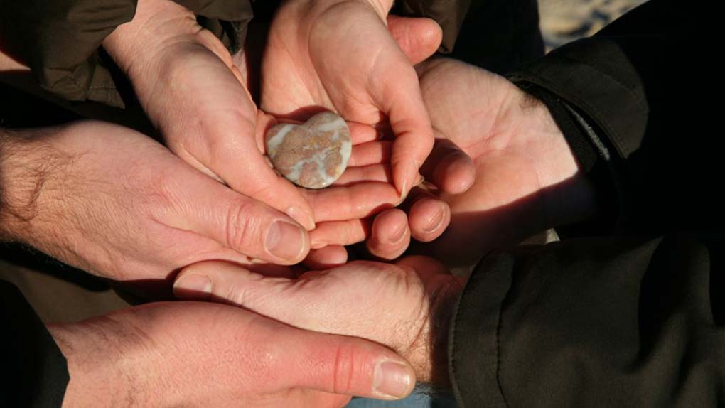 mani che tengono una pietra a forma di cuore